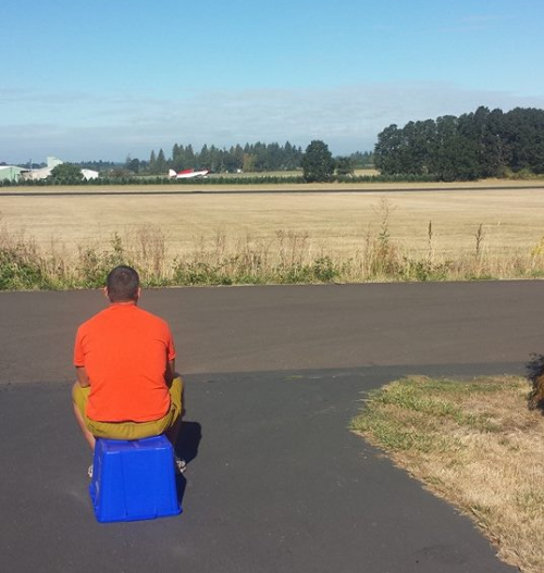 Greg sitting in front of the house watching an airplane take off